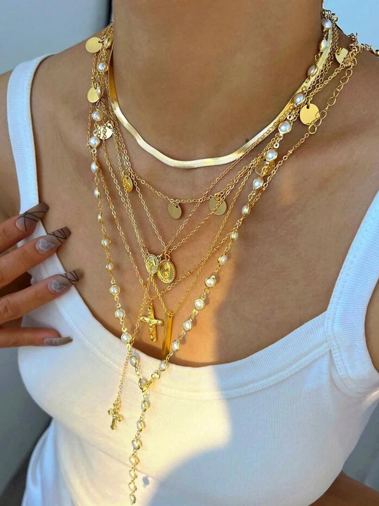 Close-up of a person wearing multiple gold necklaces with various pendants on a white background.