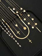 A set of gold and pearl religious necklaces and bracelets arranged on a black tray, featuring crosses, medallions, and bar charms.