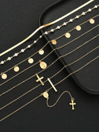 A set of gold-toned religious jewelry pieces, including necklaces with crosses, rosary-style chains, round and oval medallions, and pearl accents, arranged on a black surface next to a black jewelry box.