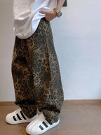 Person wearing leopard print pants and white Adidas shoes against a plain background