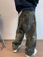 Person wearing leopard print pants and a dark top against a plain wall.