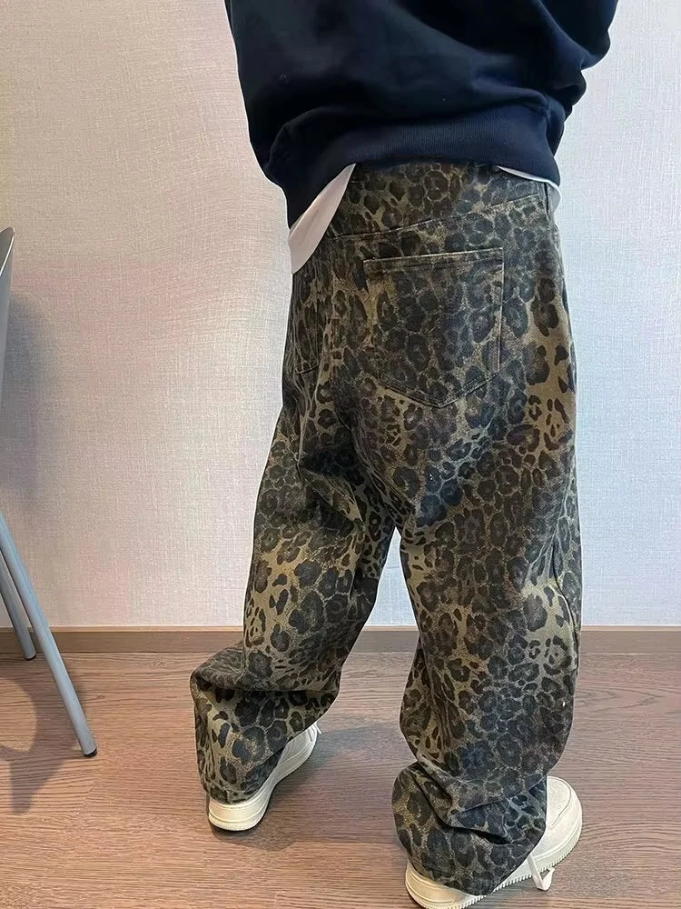 Person wearing leopard print pants and a dark top against a plain wall.