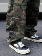 Person wearing camouflage pants and black and white sneakers on a concrete surface