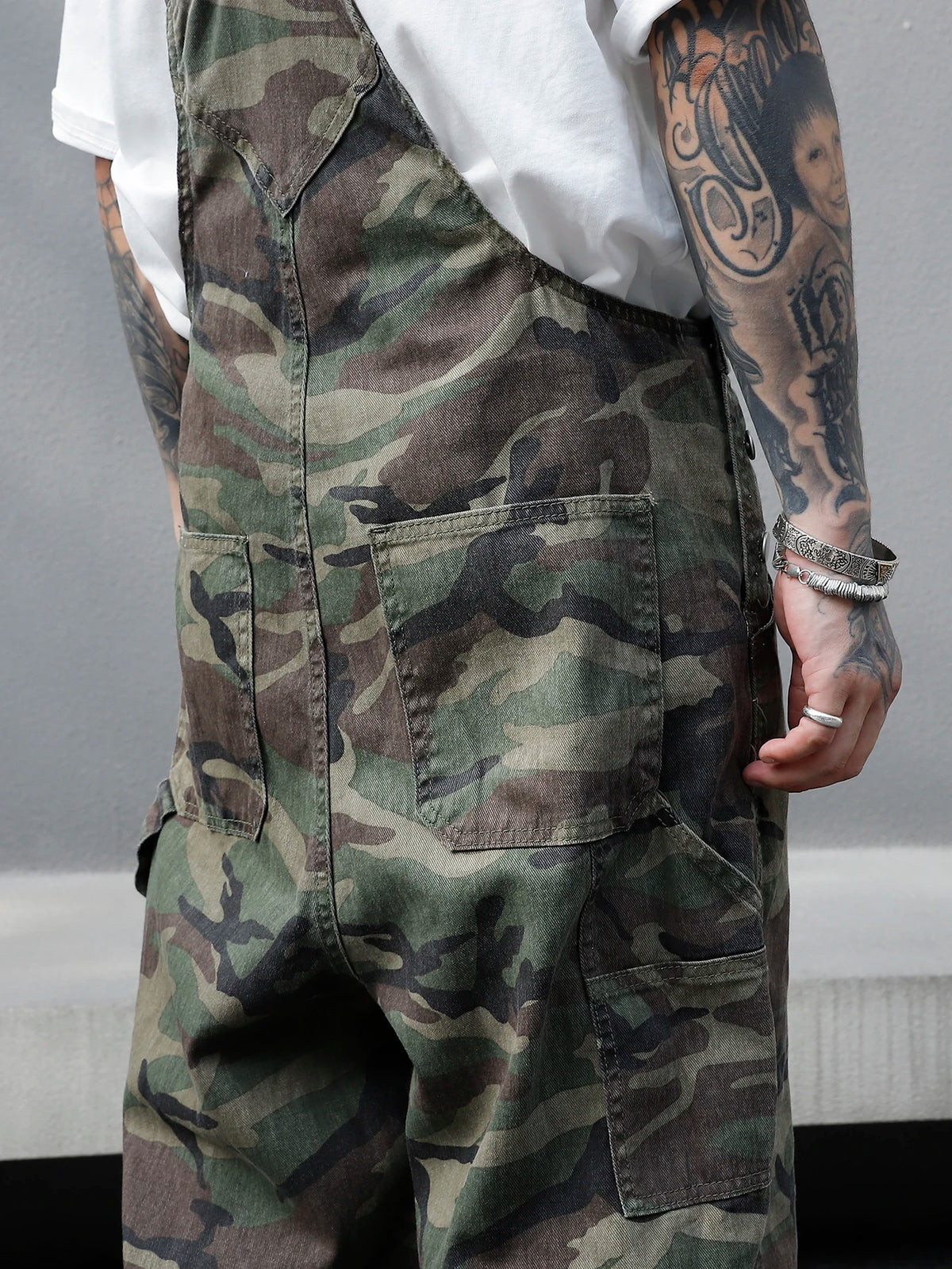 Person wearing camouflage overalls with a white shirt underneath, on a neutral background.