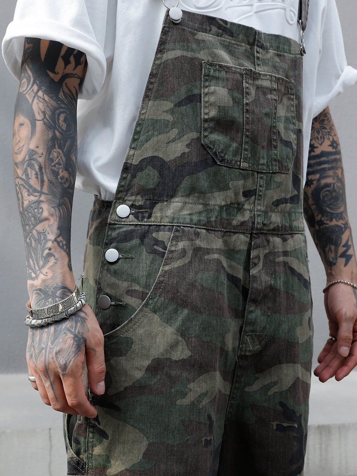 Person wearing camouflage overalls with tattoos on arms and hands.