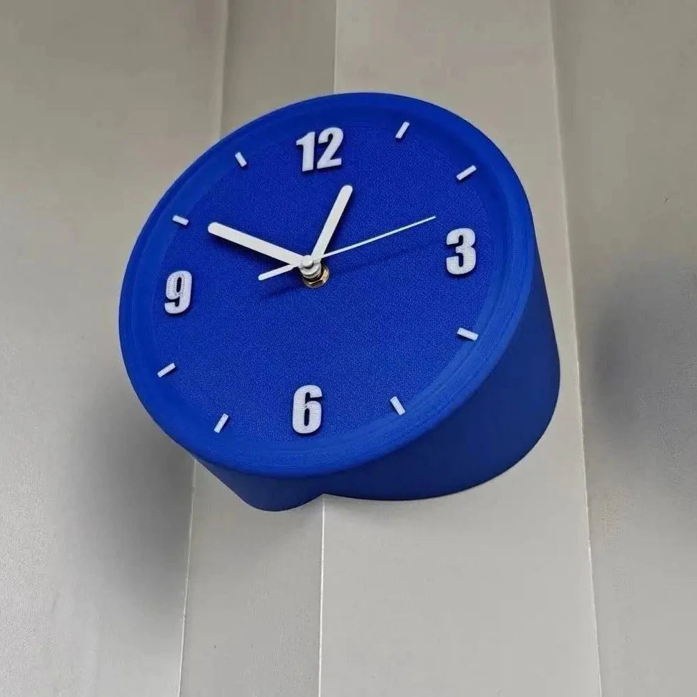 A bright blue cylindrical wall clock with white hands and white Arabic numerals, mounted on a light gray paneled wall.