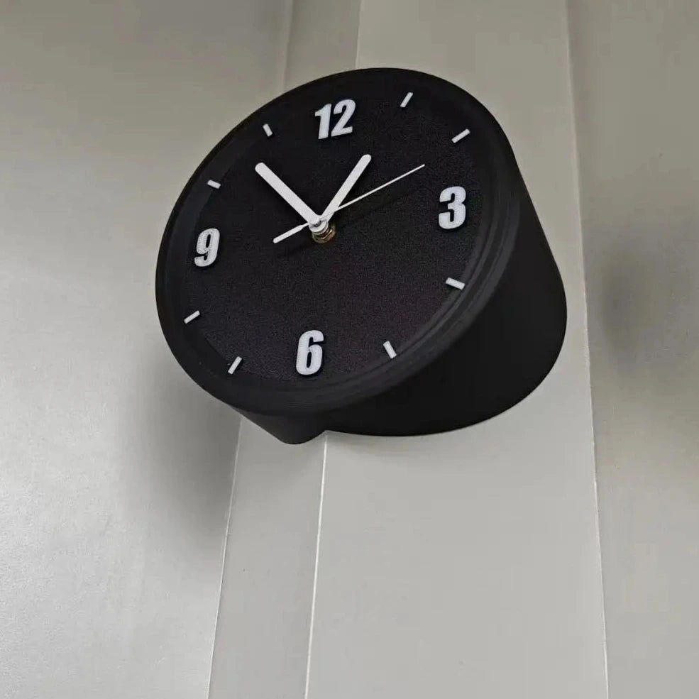 A modern black cylindrical wall clock with white numerals and hands, mounted on a light gray paneled wall.