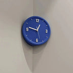 A round blue wall clock with white numerals and hands, mounted on a light gray corner wall.