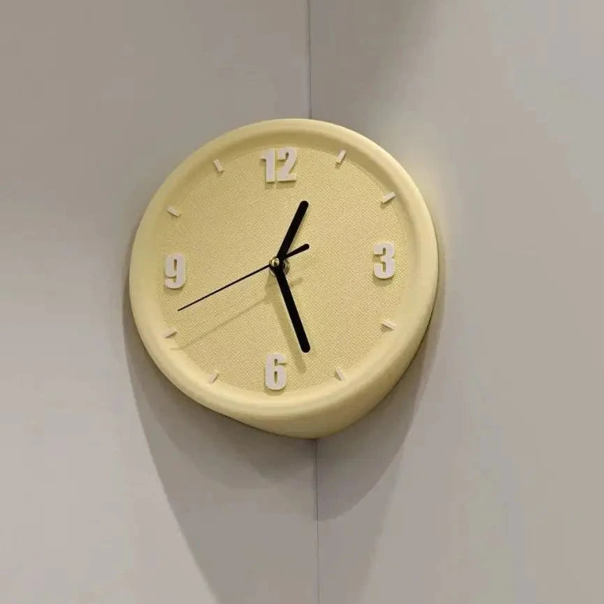 A round, asymmetrical cream-colored wall clock with black hands and white numerals, mounted on a light gray corner wall.