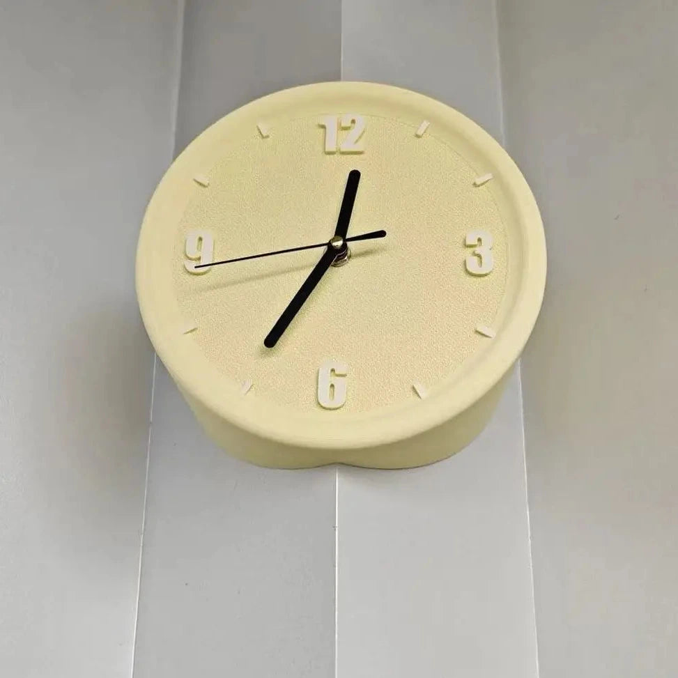 A round wall clock with a pale cream-colored textured body, black hands, and raised Arabic numerals, mounted on a white paneled wall.