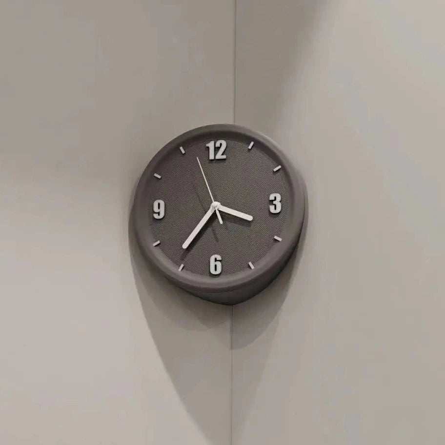 A minimalist round wall clock with a dark gray face and matching outer rim, featuring white Arabic numerals and hands, mounted on a light gray corner wall.