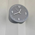 A modern round wall clock with a textured gray face and a matte gray cylindrical body, mounted on a light gray paneled wall.