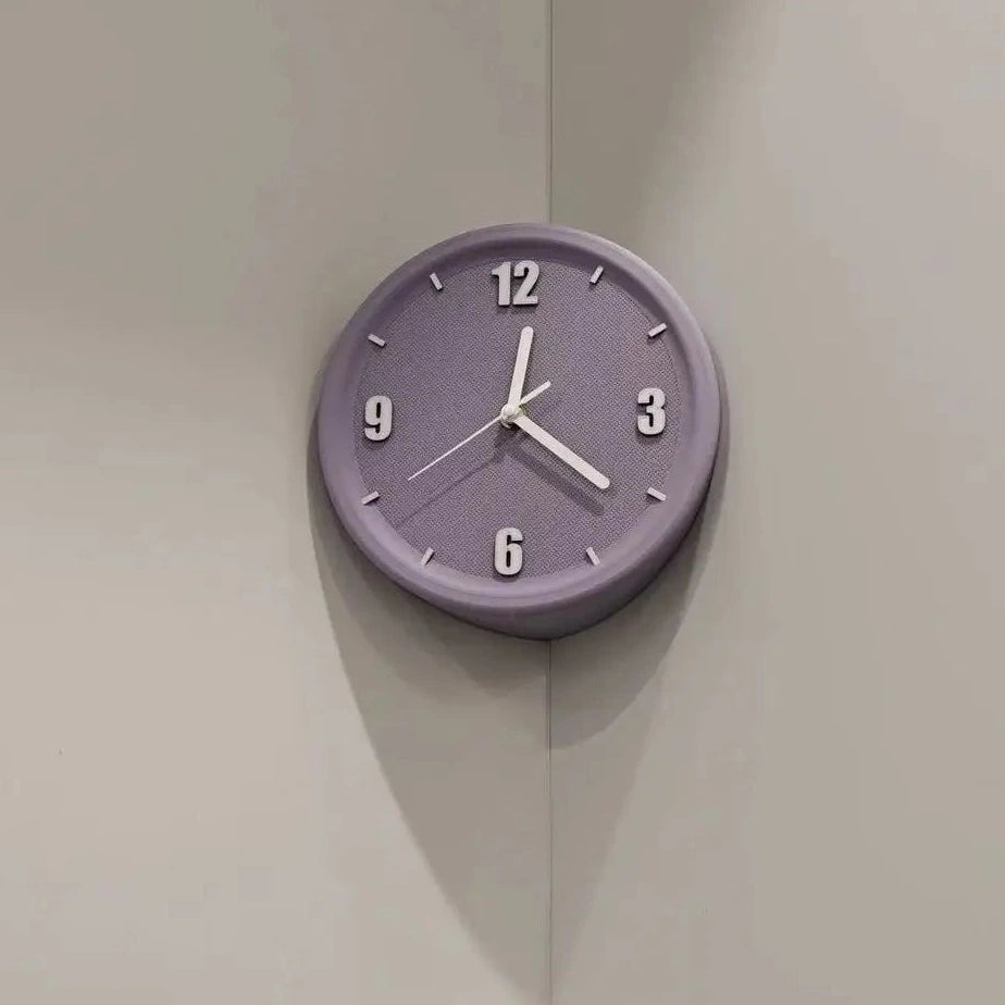 A round wall clock with a muted lavender-purple face and white hands, mounted on a light beige corner wall.