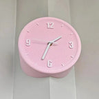 A pink heart-shaped wall clock with white hands and white Arabic numerals, mounted on a white paneled wall.