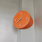 An orange wall clock with a tapered, cone-like cylindrical body and white numerals and hands, mounted on a light gray wall.
