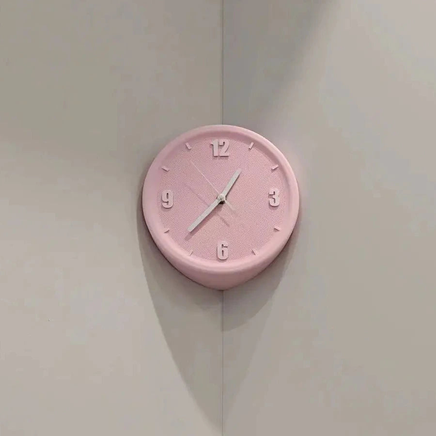 A round pink wall clock with black Arabic numerals and white hands, mounted on a light gray corner wall.