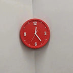 A round red wall clock with white hands and white Arabic numerals, mounted on a light gray corner wall.