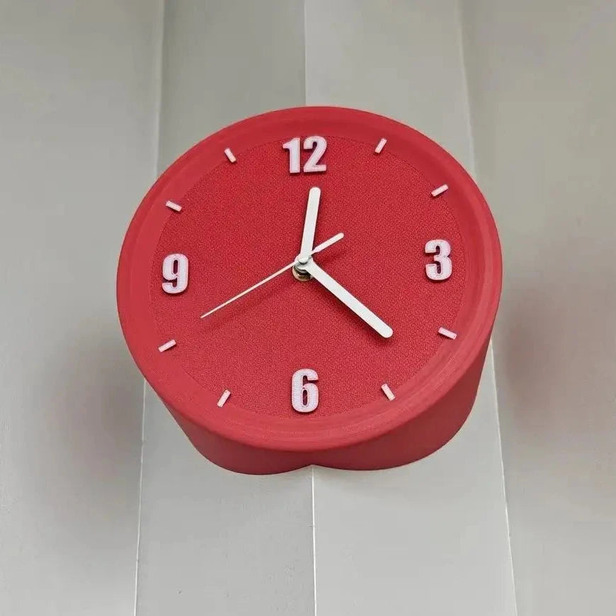 A red heart-shaped wall clock with white numerals and hands, mounted on a white paneled wall.