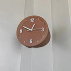 A round terracotta brown wall clock with white Arabic numerals and hands, mounted on a white paneled wall.