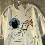 White T-shirt with cartoon cats under an umbrella design.