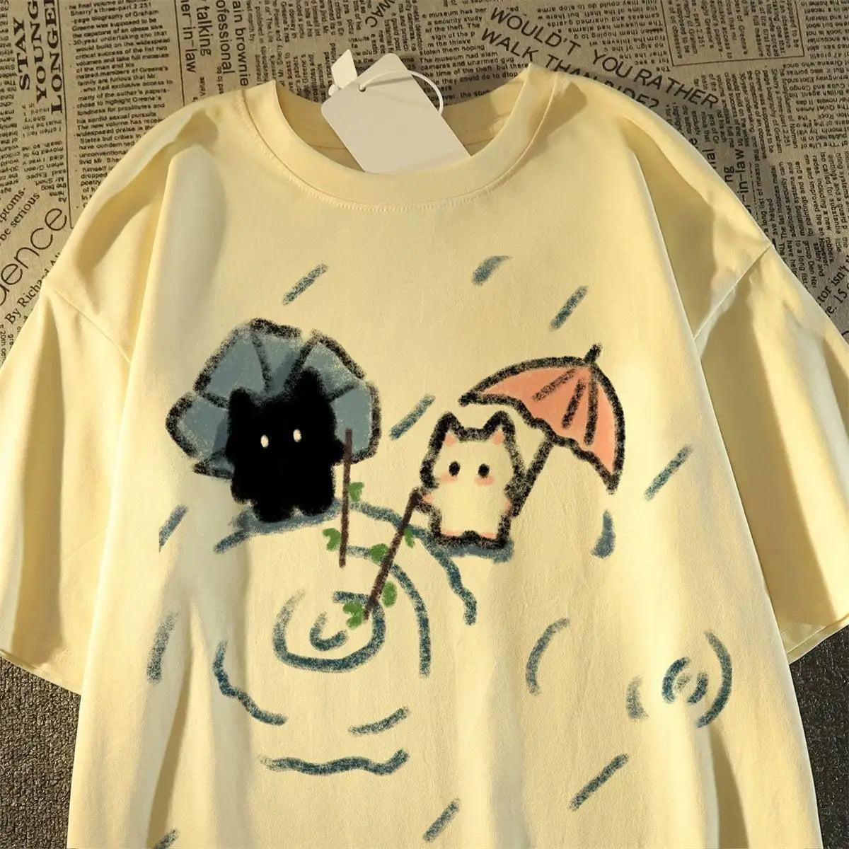 Yellow t-shirt with cat cartoon characters holding umbrellas on a textured background