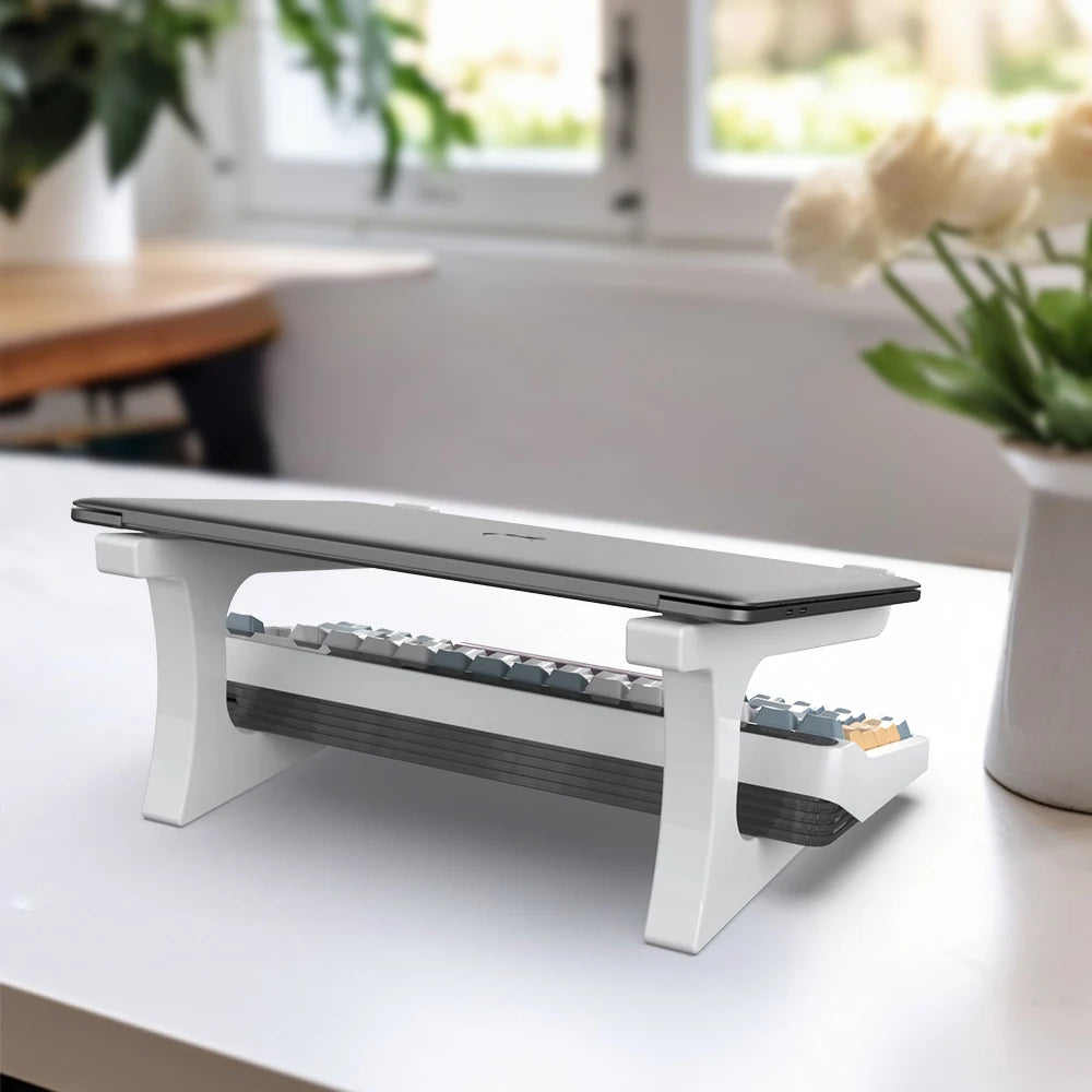 Keyboard riser on a desk with a laptop and keyboard, in a bright room with plants.