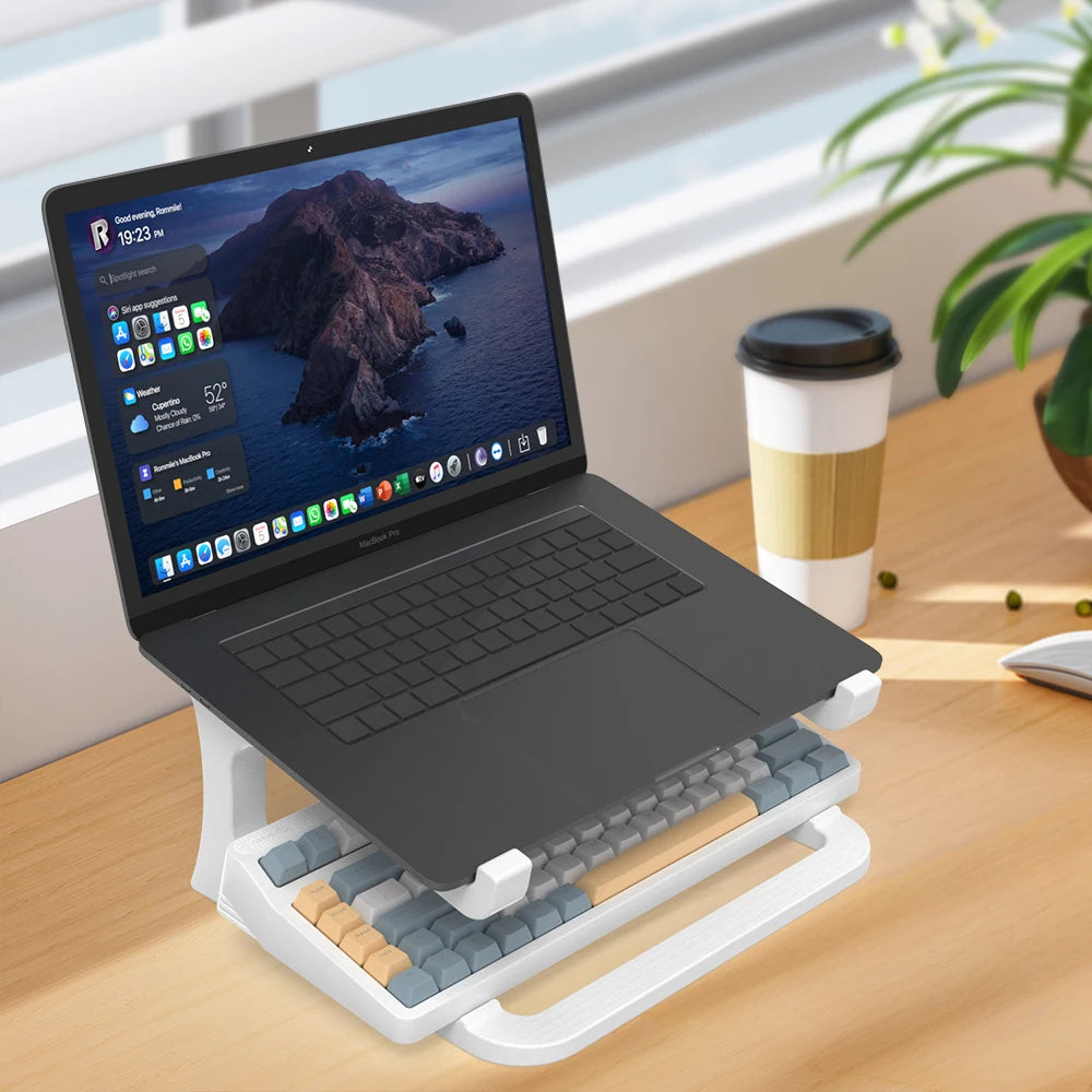 Laptop on a stand with a keyboard and mouse on a desk, next to a coffee cup and plant.