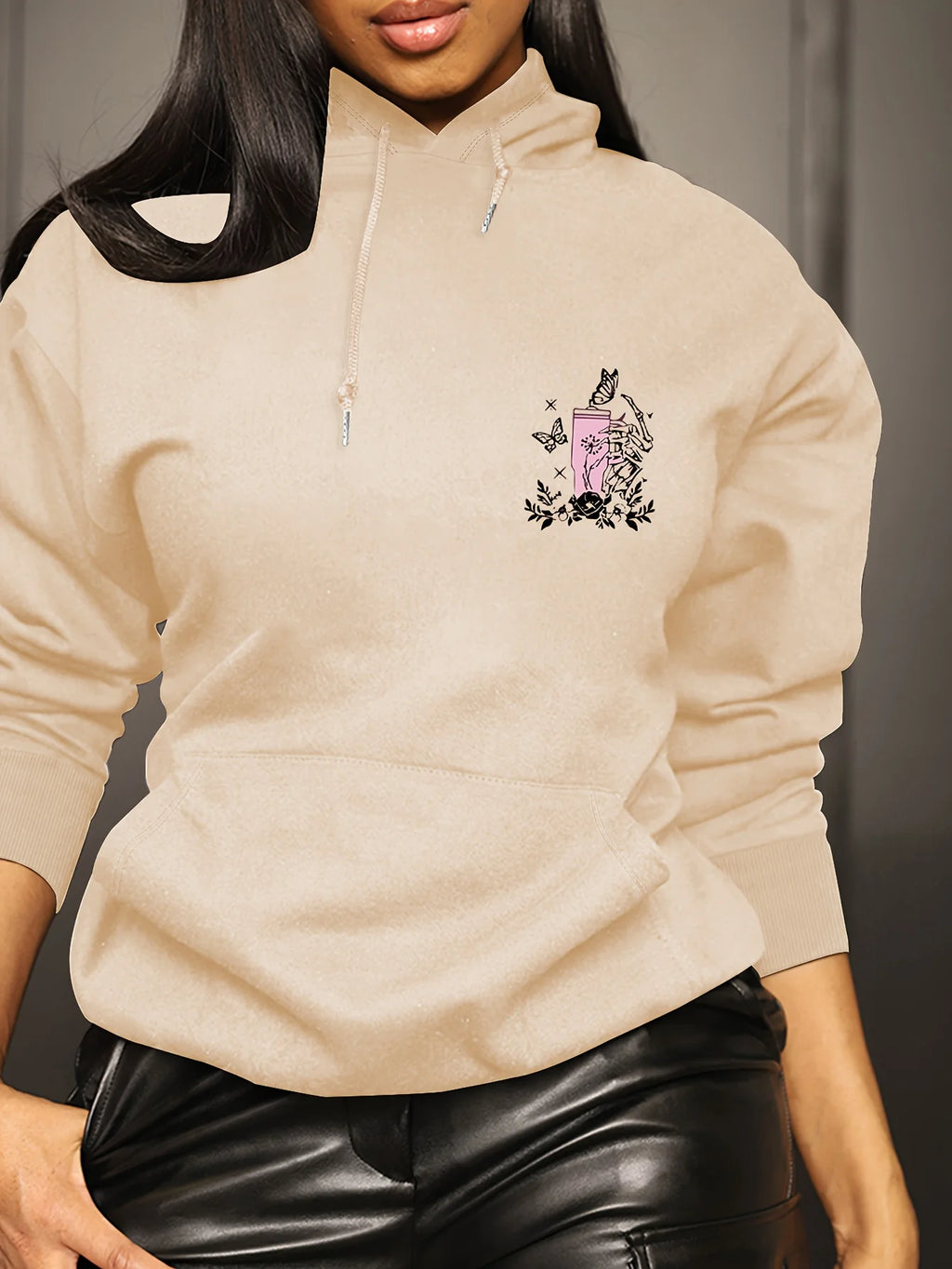 A woman wearing an ivory vintage white hoodie with a small pink and black graphic on the left chest, paired with black leather pants.