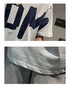 White t-shirt with navy blue lettering and gray pants on a neutral background