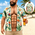 A man on a beach wearing a short-sleeve open button-up Hawaiian shirt with a tropical floral print. The shirt has green palm leaves and orange, red, and white flowers on a light beige background.
