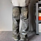 Person wearing gray jeans with graffiti-style text in a room with a shelf in the background.