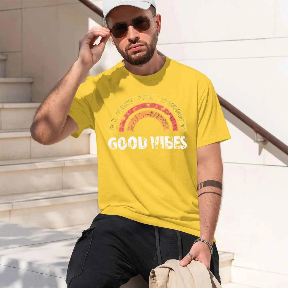 A man wearing a yellow graphic t-shirt with a distressed rainbow and the words 'GOOD VIBES' in white.