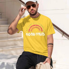 A man wearing a yellow graphic t-shirt with a distressed rainbow and the words 'GOOD VIBES' in white.
