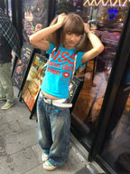 Woman wearing a blue Kiss T-shirt Fashion Vintage Harajuku Streetwear blue and jeans standing on a sidewalk.