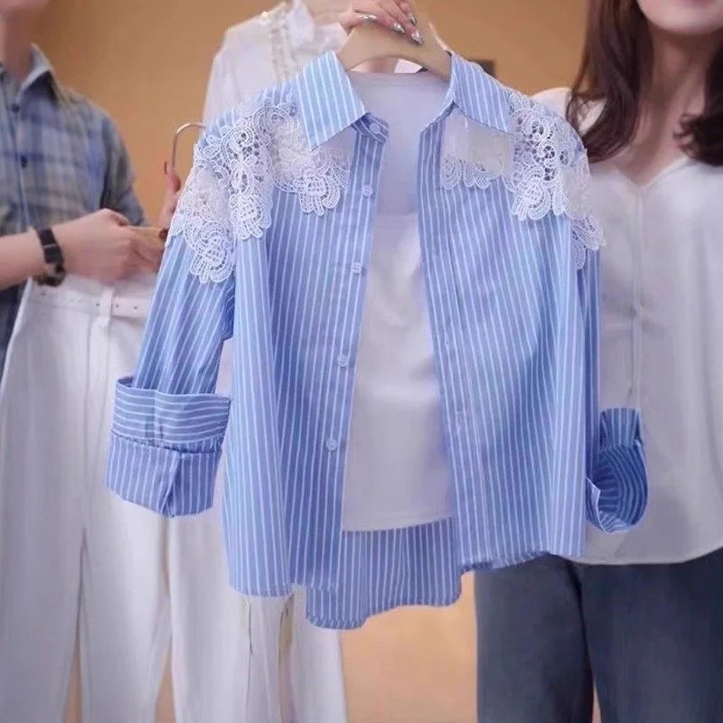 A blue and white vertically striped button-up shirt with white floral lace applique on the shoulders, held on a wooden hanger by a person in a white top. Other people are partially visible in the background.