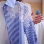 A close-up of a blue and white striped long-sleeve shirt with a large white lace applique detail across the chest, worn by a person whose hand is visible gesturing near the shoulder.