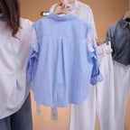 A person holds up a light blue and white vertically striped blouse with white lace sleeves, showing the back of the shirt. Other clothing items are hanging in the background.