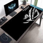 A black desk mat with a white Republic of Shadows logo and text, laid out on a wooden desk in a modern home office setup alongside a computer monitor, mouse, and headset.