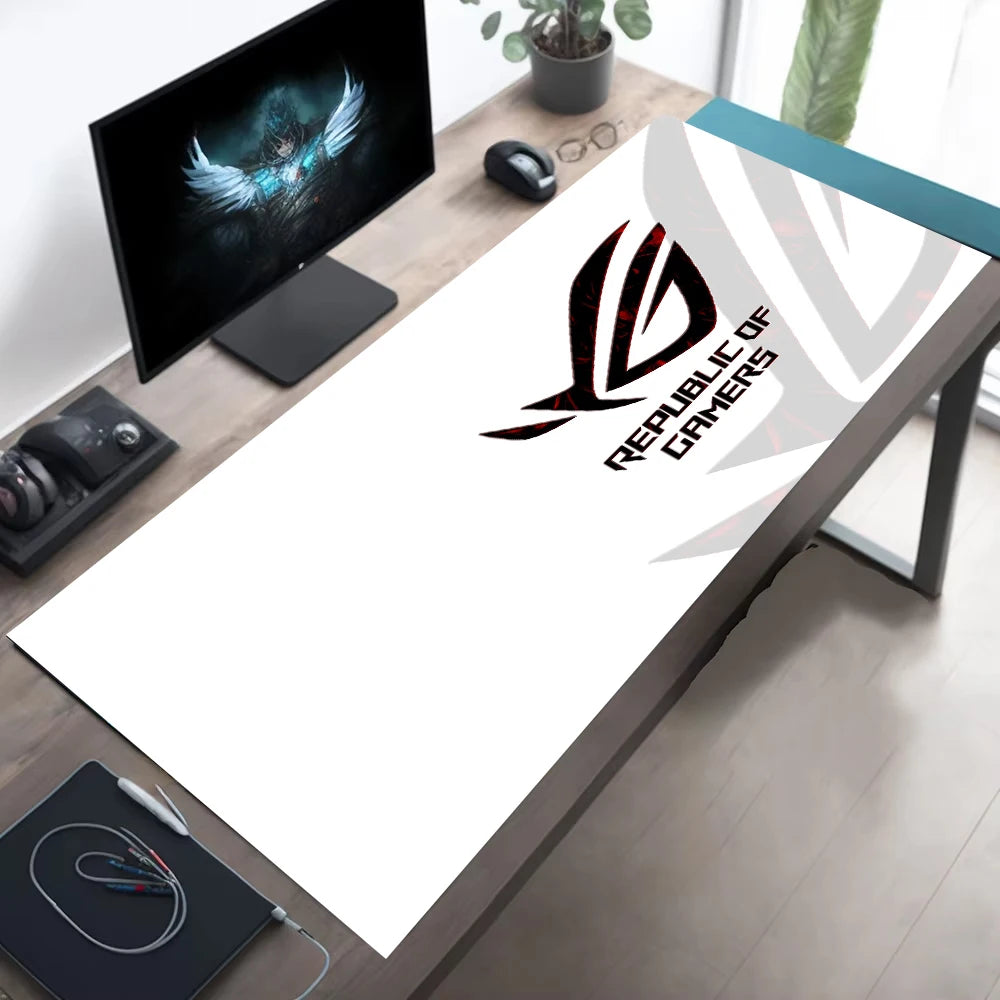 A large white desk mat featuring the black and red Republic of Gamers logo, displayed on a wooden gaming desk alongside a computer monitor, mouse, and headset.