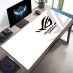 A large white desk mat featuring the black and red Republic of Gamers logo, displayed on a wooden gaming desk alongside a computer monitor, mouse, and headset.