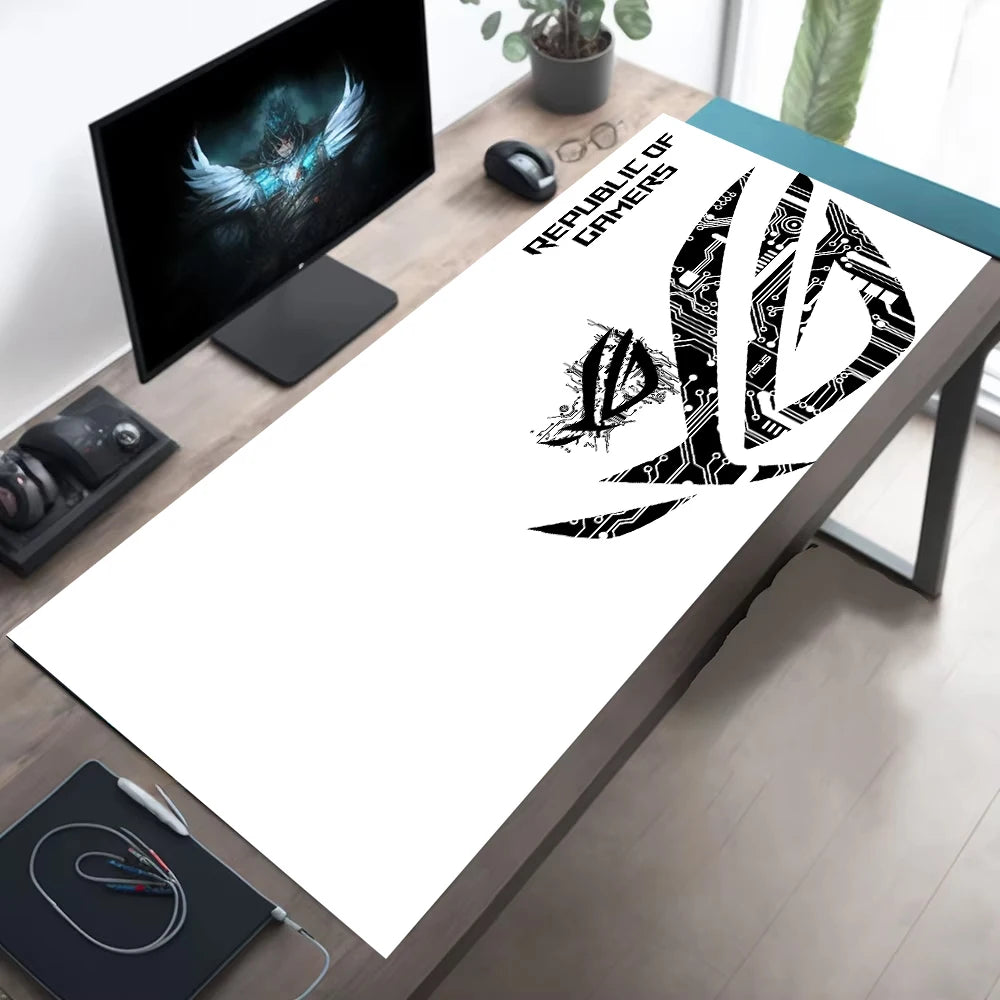 A large white desk mat with a black ASUS ROG 'Republic of Games' logo and text, laid out on a wooden desk in a modern home office setup.
