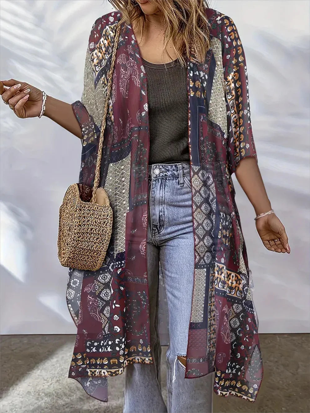 Woman wearing a long, patterned kimono-style garment with light blue jeans against a white background.