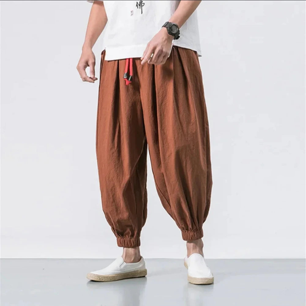 Person wearing brown baggy pants and white shoes on a plain background