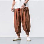 Person wearing brown baggy pants and white shoes on a plain background