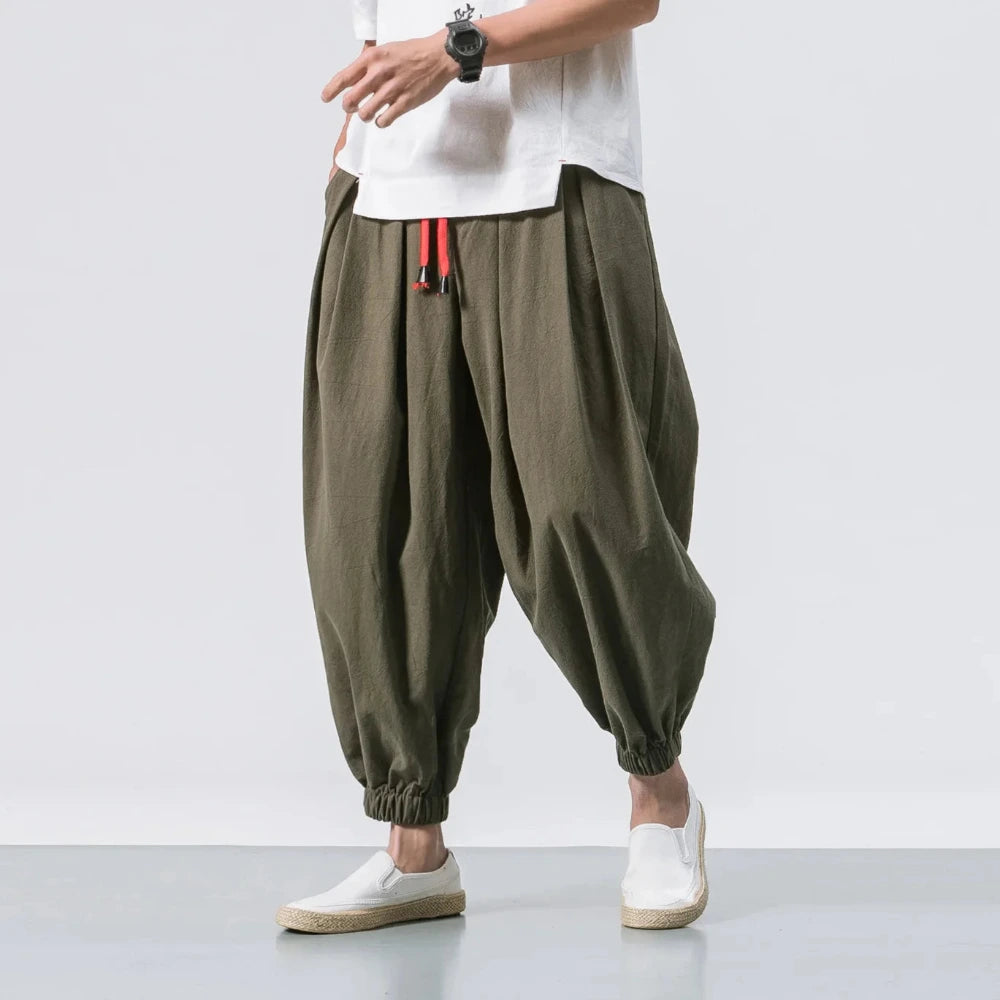 Person wearing olive green baggy pants with a white shirt and white shoes on a light gray background