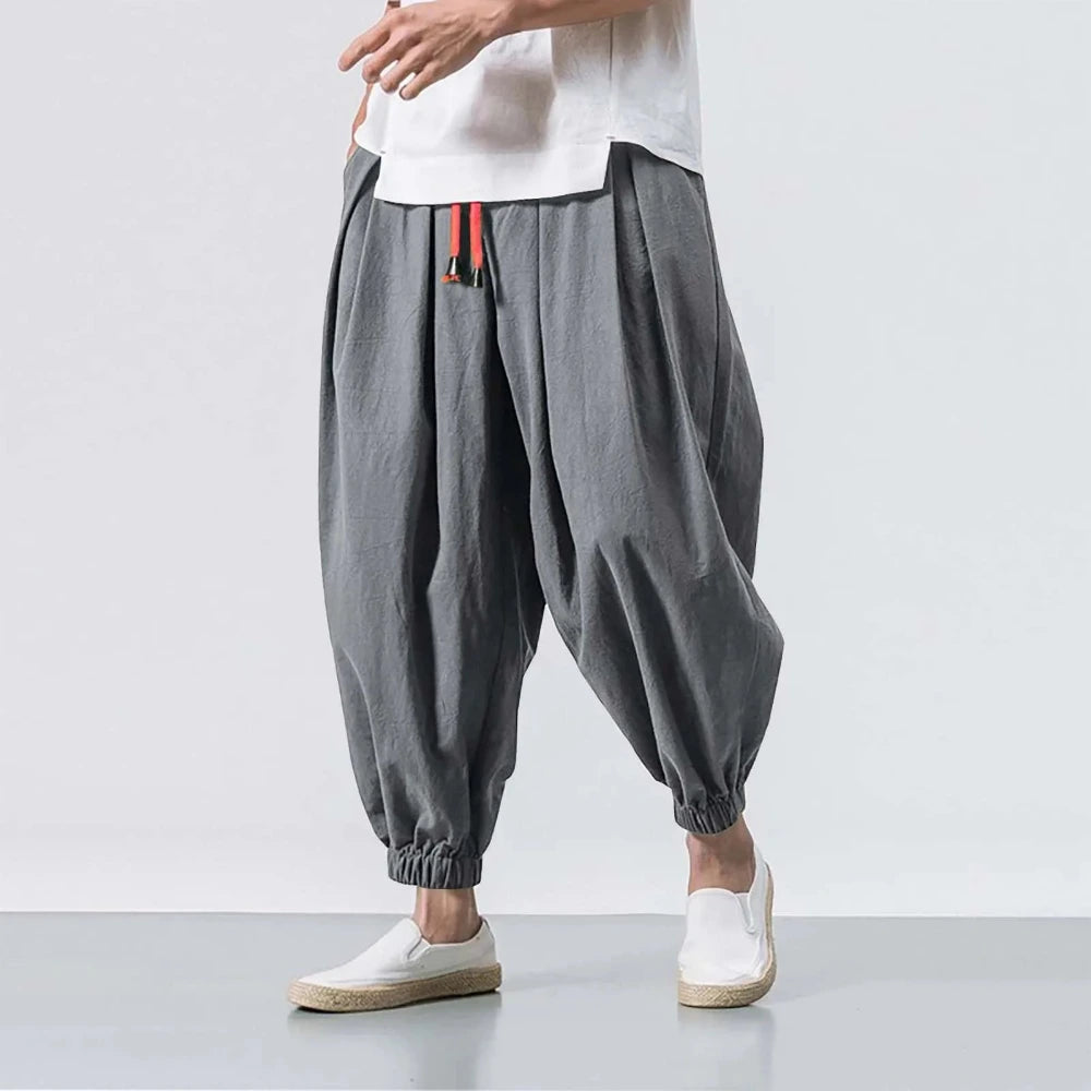 Person wearing gray harem pants and white shoes on a light gray background