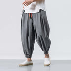 Person wearing gray harem pants and white shoes on a light gray background