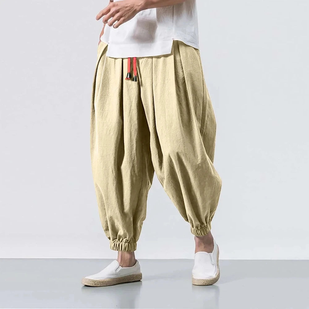 Beige harem pants worn with a white shirt on a plain background