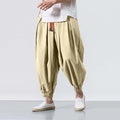 Beige harem pants worn with a white shirt on a plain background