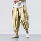Beige harem pants worn with a white shirt on a plain background